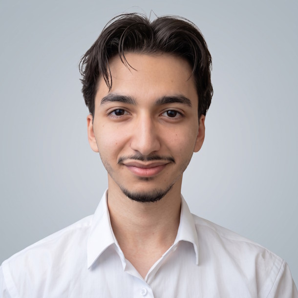 A professional headshot of Karim Alkaddi, consultant at Decision Lab Ltd. He is a man with a slight beard, dark hair, and brown eyes. He wears a white shirt against a neutral grey-blue background and is looking directly at the camera with a subtle smile.